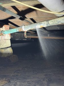 A galvanized pipe leak spraying under a home with a crawl space on a St Petersburg leak detection job service.